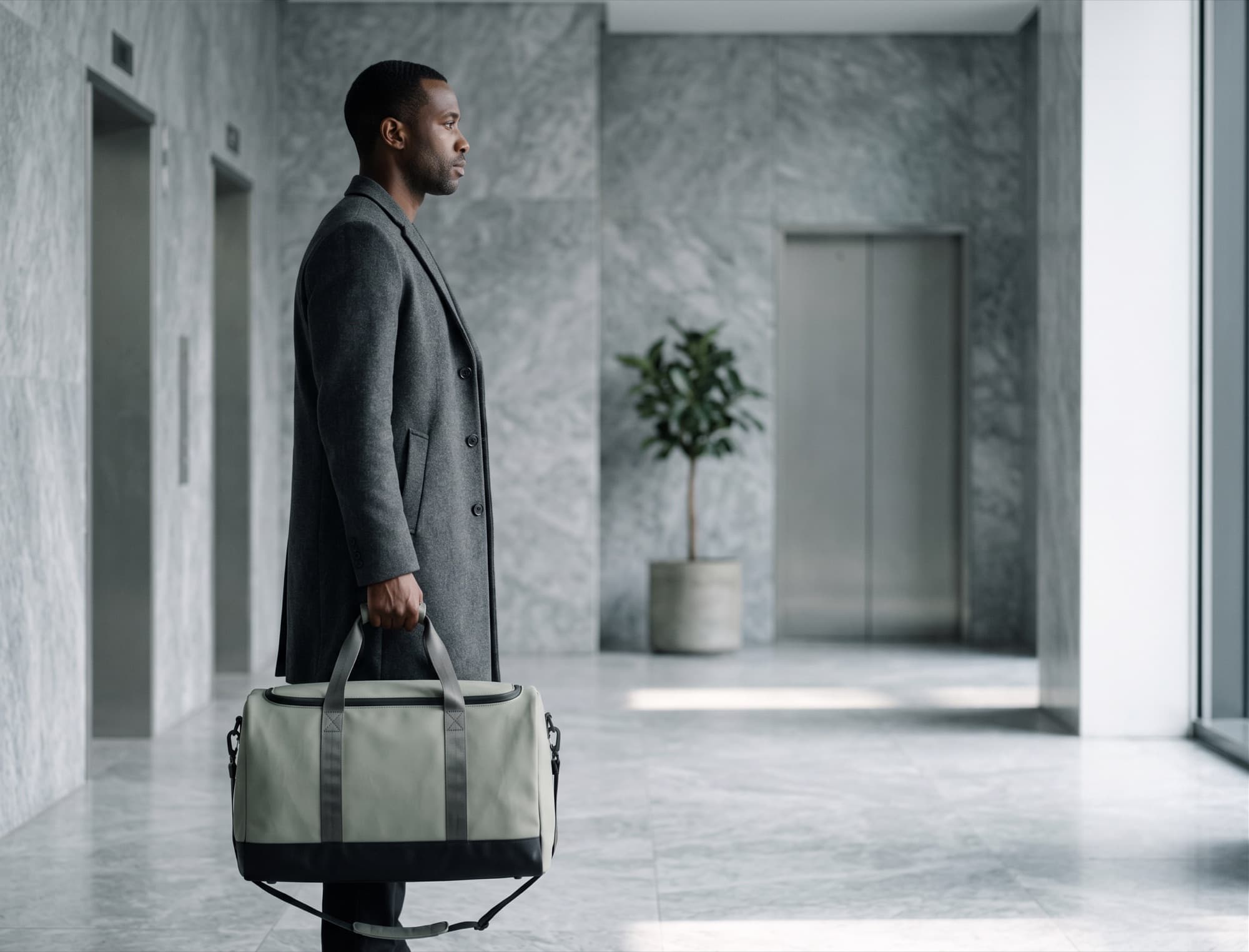 Waiting in a marble lift lobby, bag held at the side